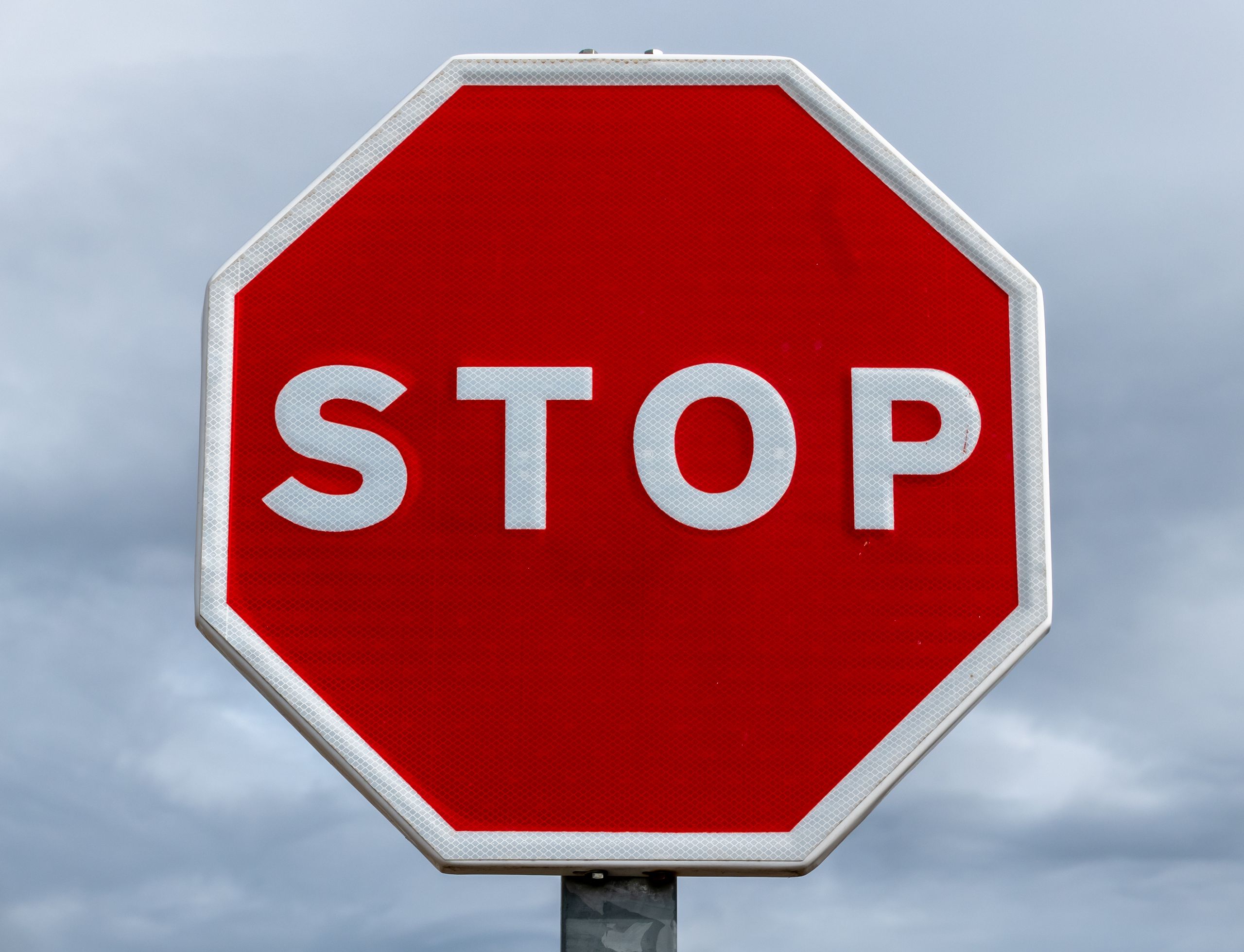 Close-up of a red stop sign with a cloudy sky backdrop, highlighting traffic regulation.